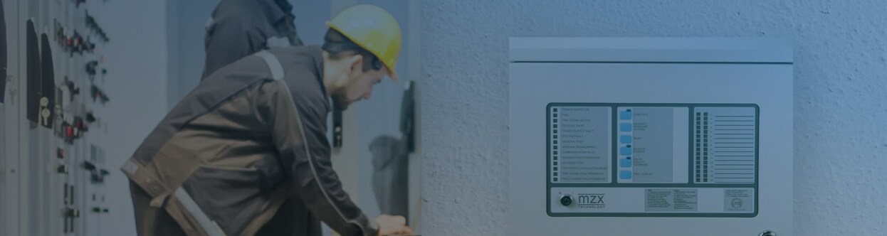 Two electrical engineers at work in a facility, with a fire control panel in the foreground