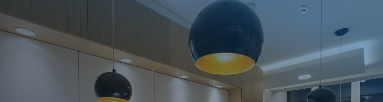 Fire detectors mounted on a ceiling near hanging lights